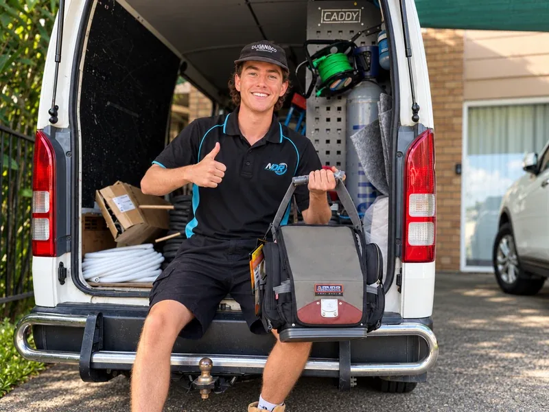 A smiling technician in NDR’s black-and-blue uniform giving a thumbs-up at a work van