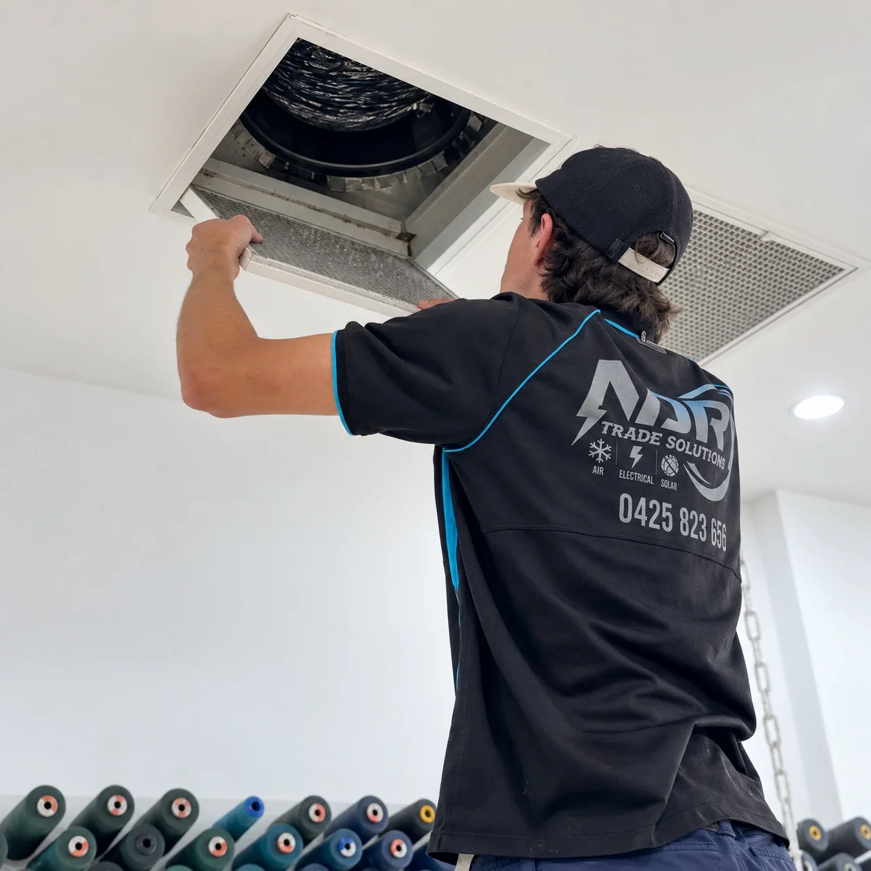 An NDR technician working on a ducted air-conditioning ceiling grille